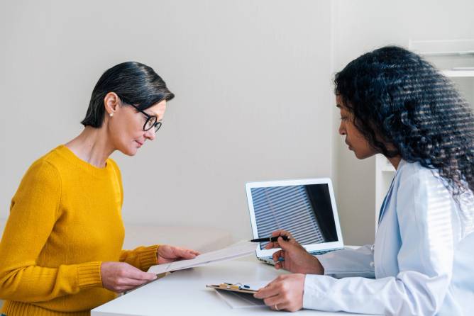 An African-American doctor is helping a female patient in a yellow sweater read through a form.