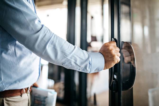 Business man opening door of office building.