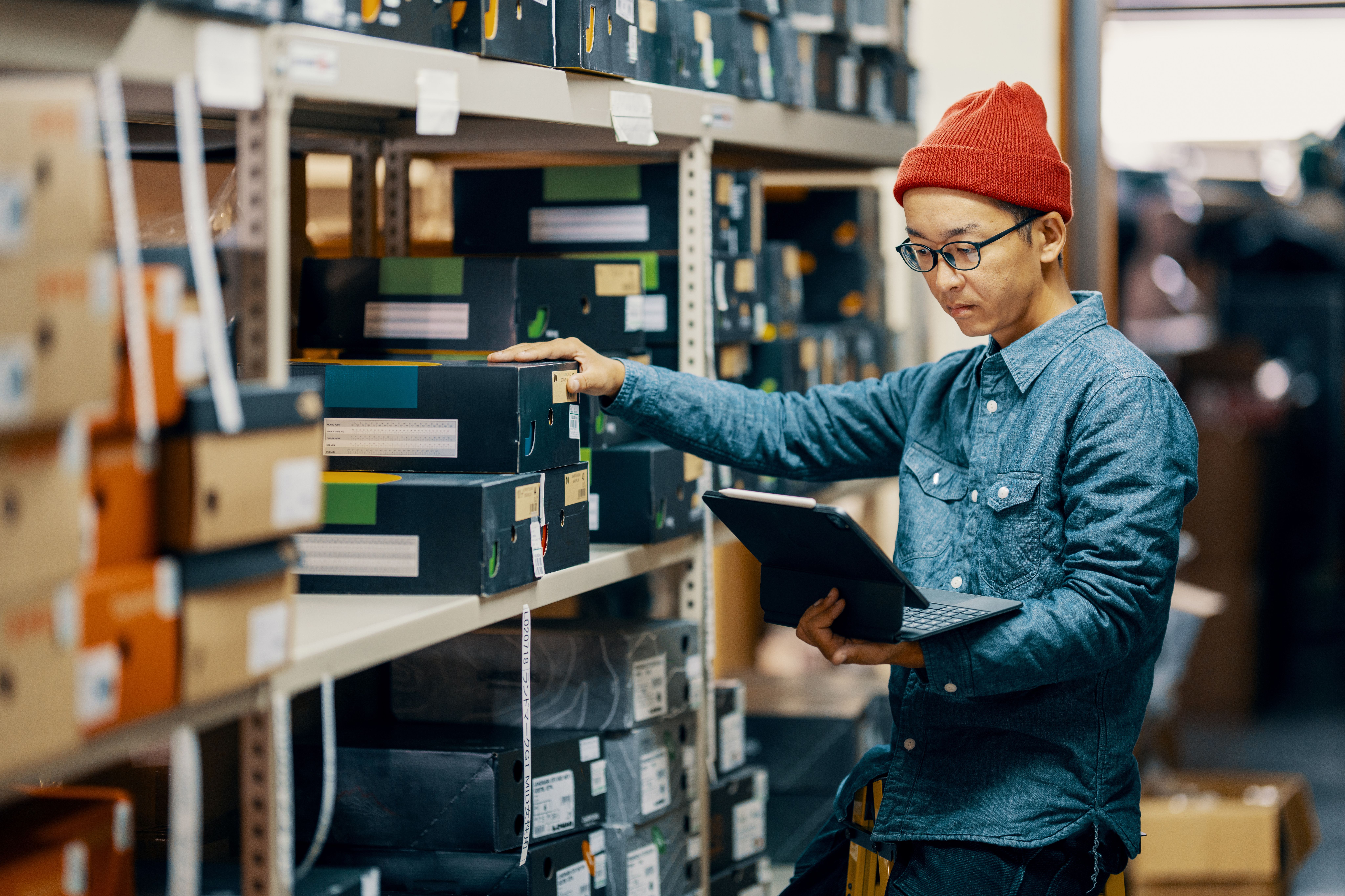 Man using computer to check inventory of shoes in a stockroom.
