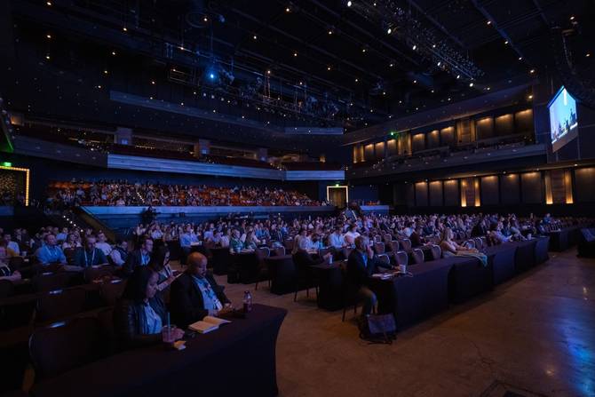 wide-angle view an audience sitting in a large auditorium with dim lighting