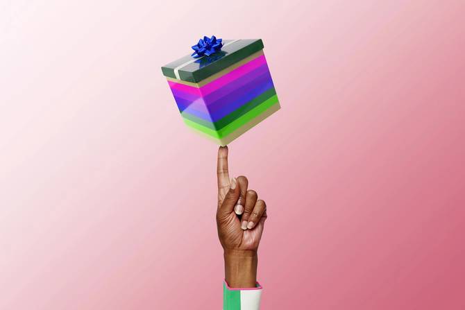 a person's hand holding up a gift on a pink background