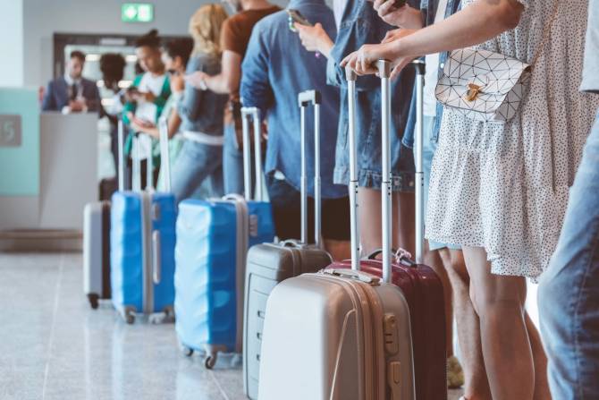 a line of blue, gray, and brown suitcases with people standing alongside of them inside of an airport 