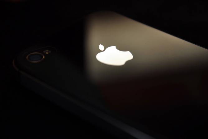 An iPhone mostly in shadow against a dark background with the Apple logo harshly illuminated