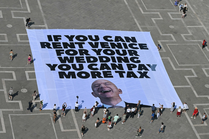 Activists of international environmental group Greenpeace deploy a giant banner displaying a picture of Jeff Bezos and reading "If you can rent Venice for your wedding you can pay more tax"