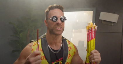 A man wearing glasses and a sleeveless vest holding up a bunch of Slim Jims