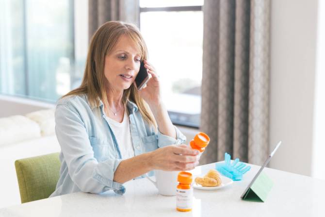 A woman is on the phone while looking at two orange pill bottles.