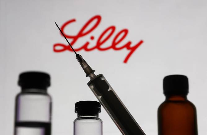 A syringe in front of vials and an Eli Lilly sign.