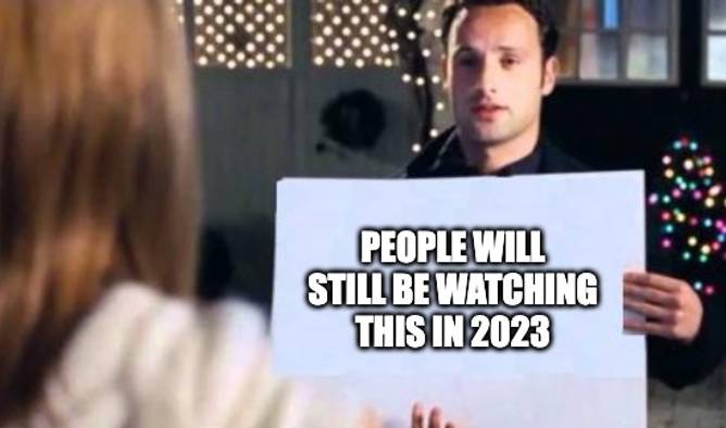 Scene in Love Actually where man holds sign that reads “pretend its carolers” but the text is replaced by “people will still be watching this in 2023”