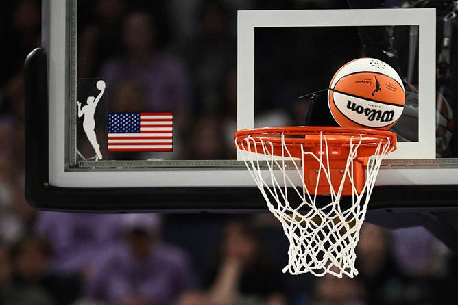 A WNBA ball going into a basket with the WNBA logo on the backboard