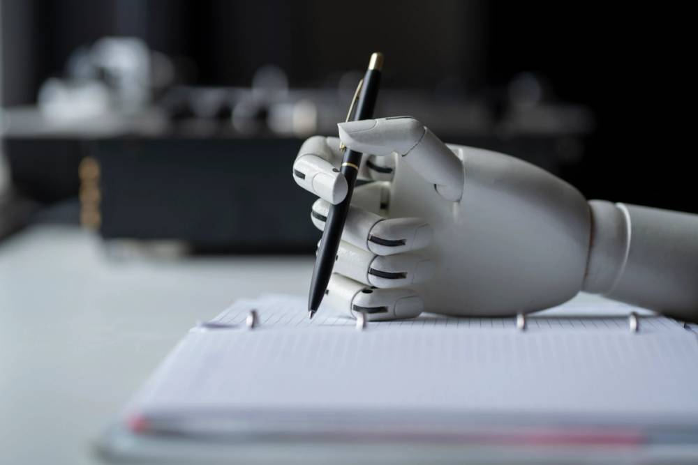 Image of a robotic hand taking notes on paper with a pen.