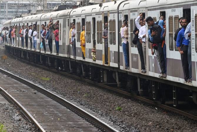 Commuters stand on open train car doors as they travel on a local train in Mumbai on September 8, 2022.