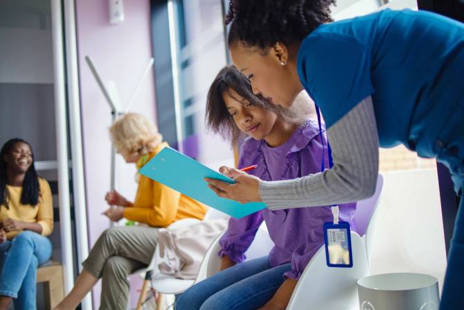 A nurse helps a young patient fill out a form.