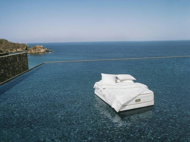 A hotel bed floating in an infinity pool overlooking the ocean.