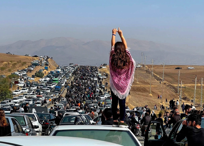 An unveiled woman stands atop a car and looks out over protests in Iran