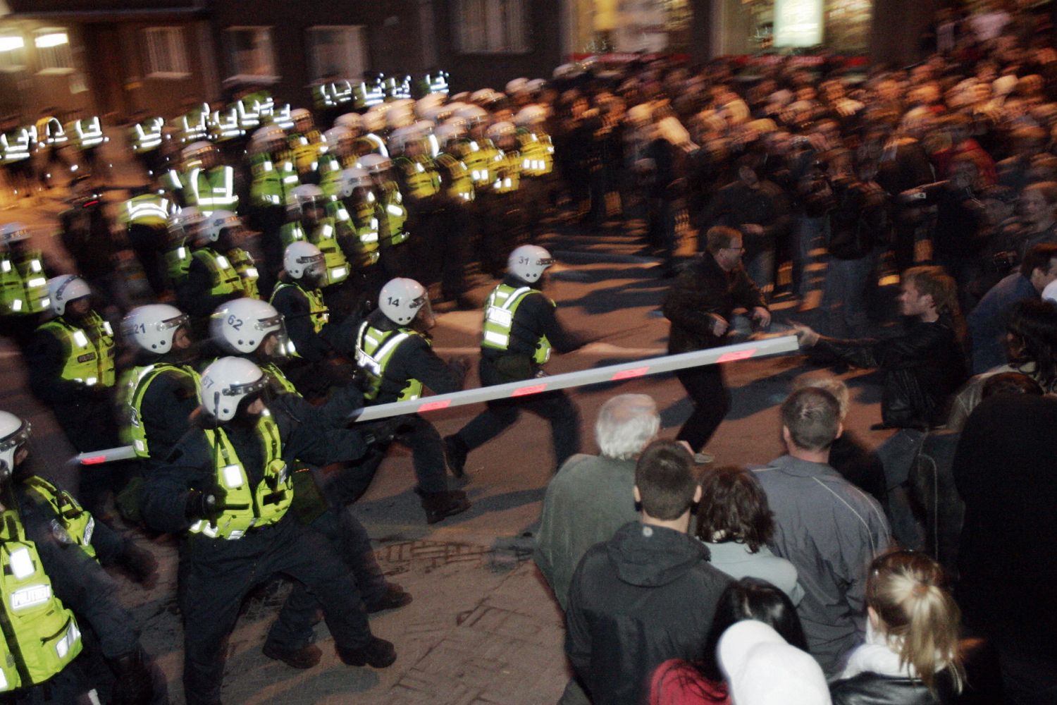 A large group of law enforcement officials in helmets and reflective gear surge forward in a crowd of bystanders
