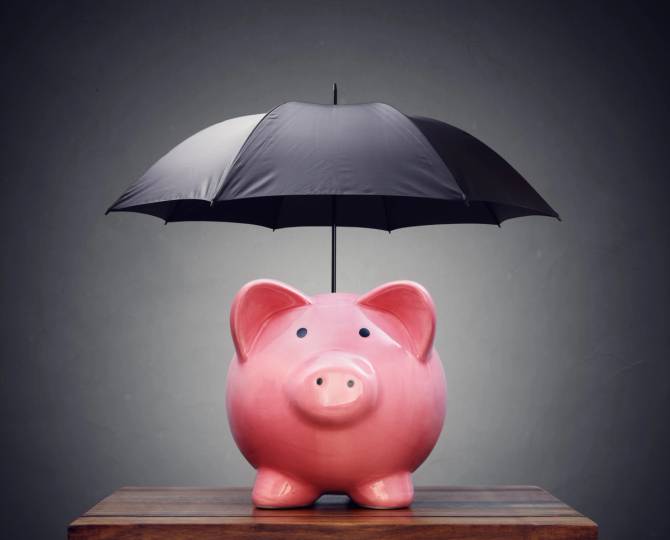 A pink piggy bank with a black umbrella standing out of the top of it sitting on a small desk with a grey background