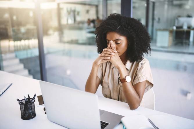 Shot of a young Black businesswoman looking stressed at her desk in a modern office.