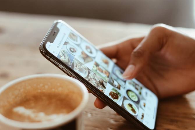a picture of a woman's hand holding a phone next to a cup of coffee