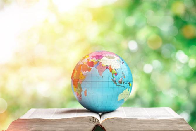 a colorful globe of earth sitting on top of an open book, with greenery behind it
