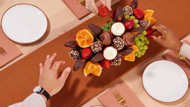 Hands reaching for the food items in an Edible arrangement.