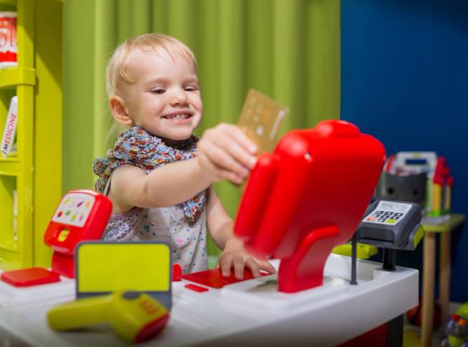 child holding a plastic credit card, pretending to swipe in a toy kitchen