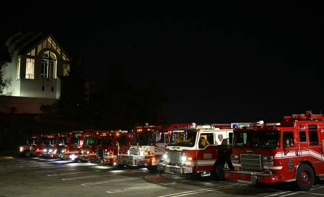 LAFD emergency vehicles and fire engines wait on stand-by on the parking lot of Bel Air Church as the Palisades Fire burns towards the Encino neighborhood in Los Angeles, California