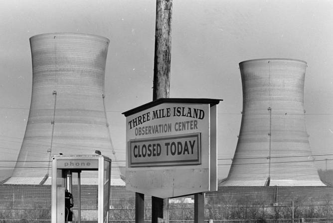 Black and white photo of Three Mile Island Observation Island sign with phone booth and two reactors in the back. Sign says the center is closed.