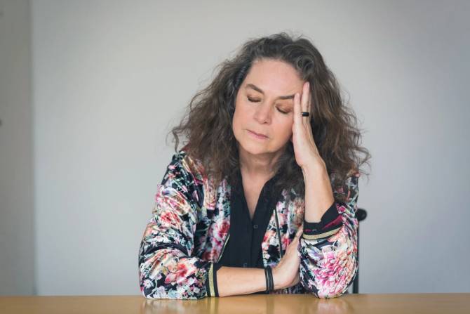 A middle aged woman closes her eyes and brings her hand to her head.