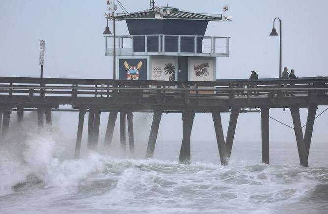 People stand on a pier over the Pacific Ocean with Tropical Storm Hilary approaching in San Diego County