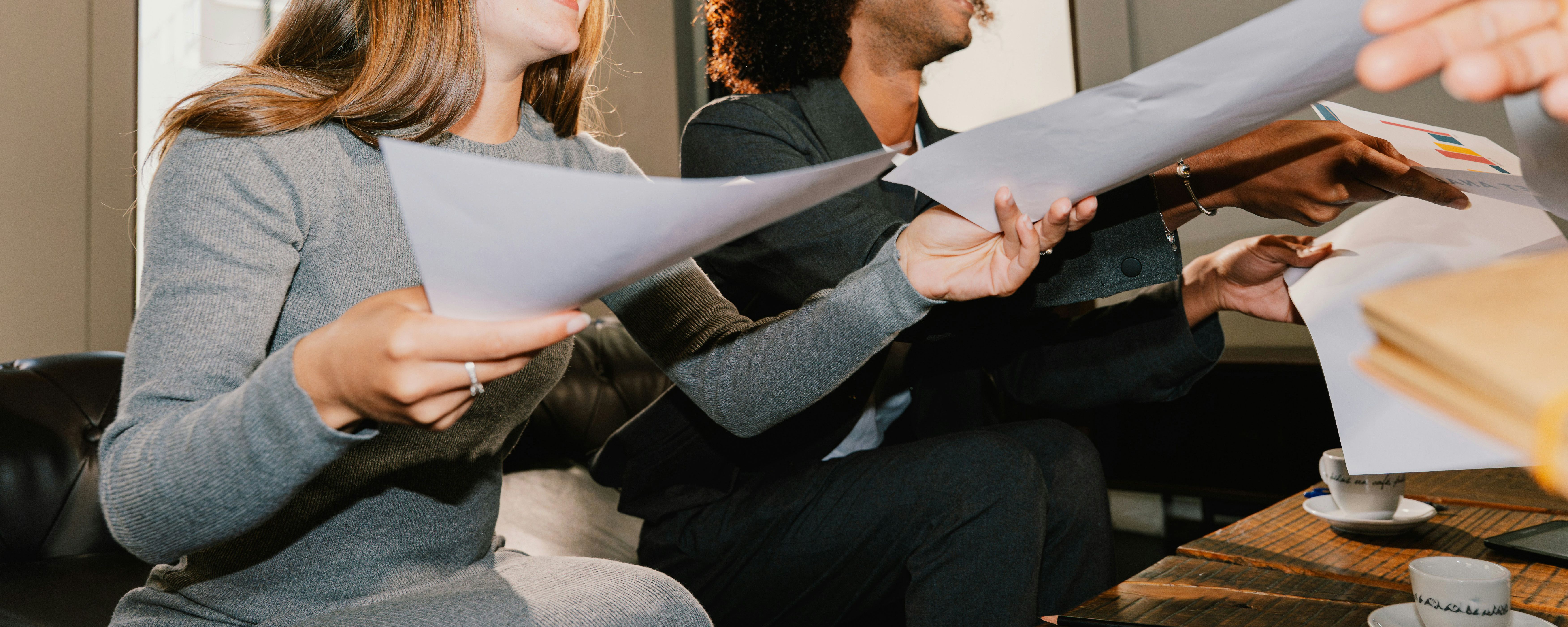 Two colleagues passing documents to each other during a meeting.