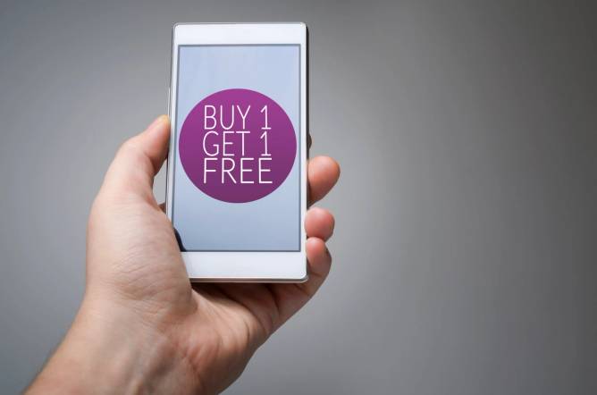 Hand holding a smartphone with buy 1, get 1 free on it