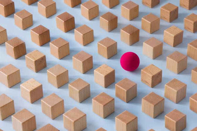 A bunch of identicalwooden blocks in a pattern with a red ball among them. 
