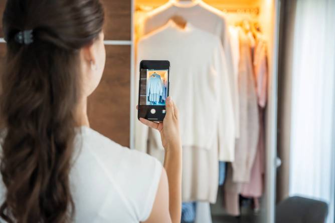 Young woman taking photos of secondhand clothes for sale in smartphone app.