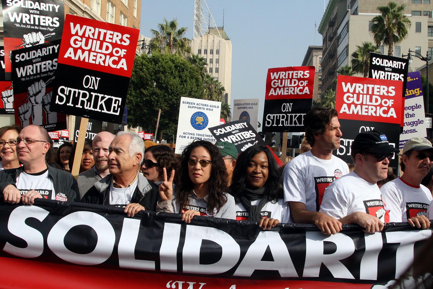 A large group of protestors, signs read 'on strike', city backdrop.