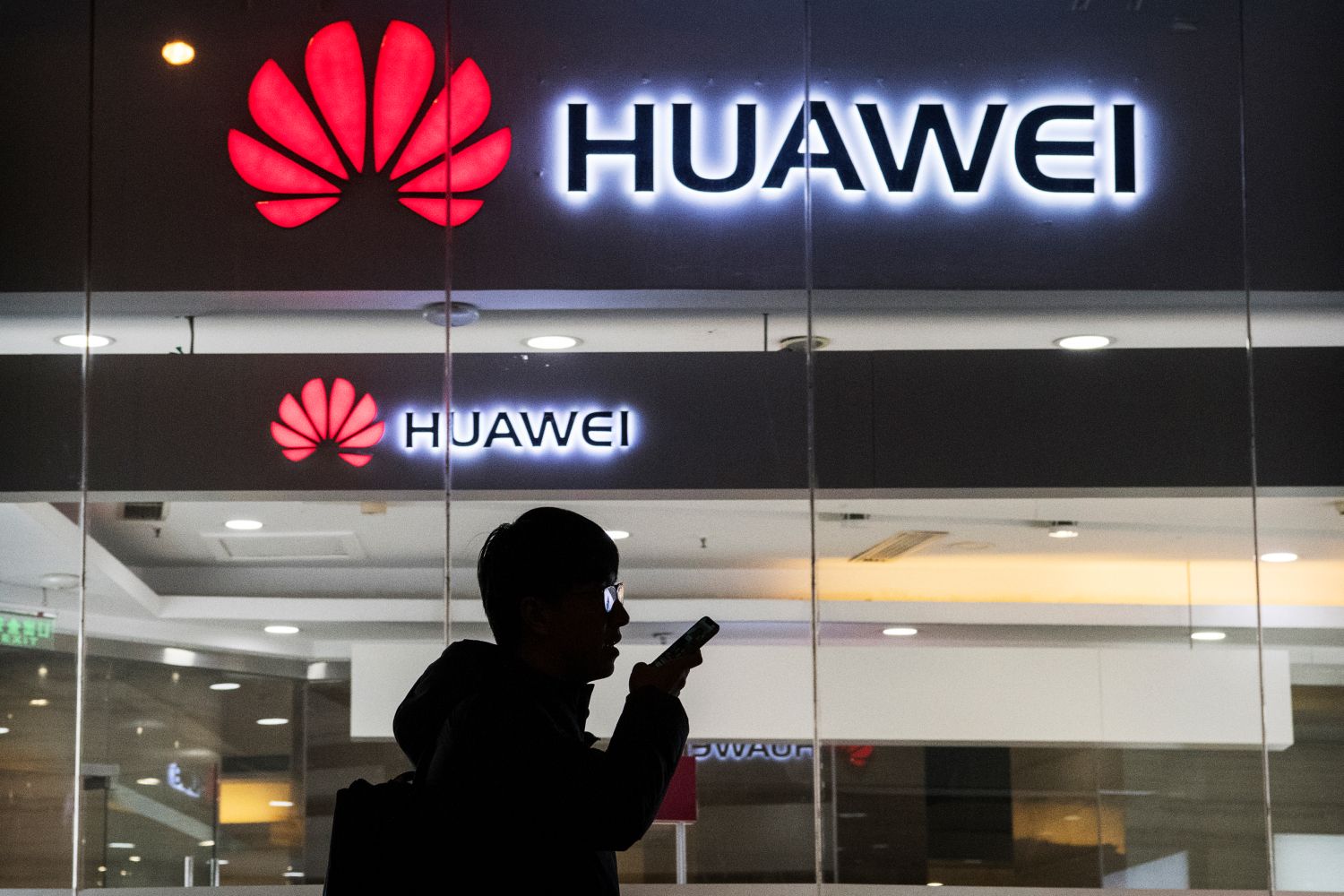 A pedestrian talks on the phone while walking past a Huawei Technologies Co. store.