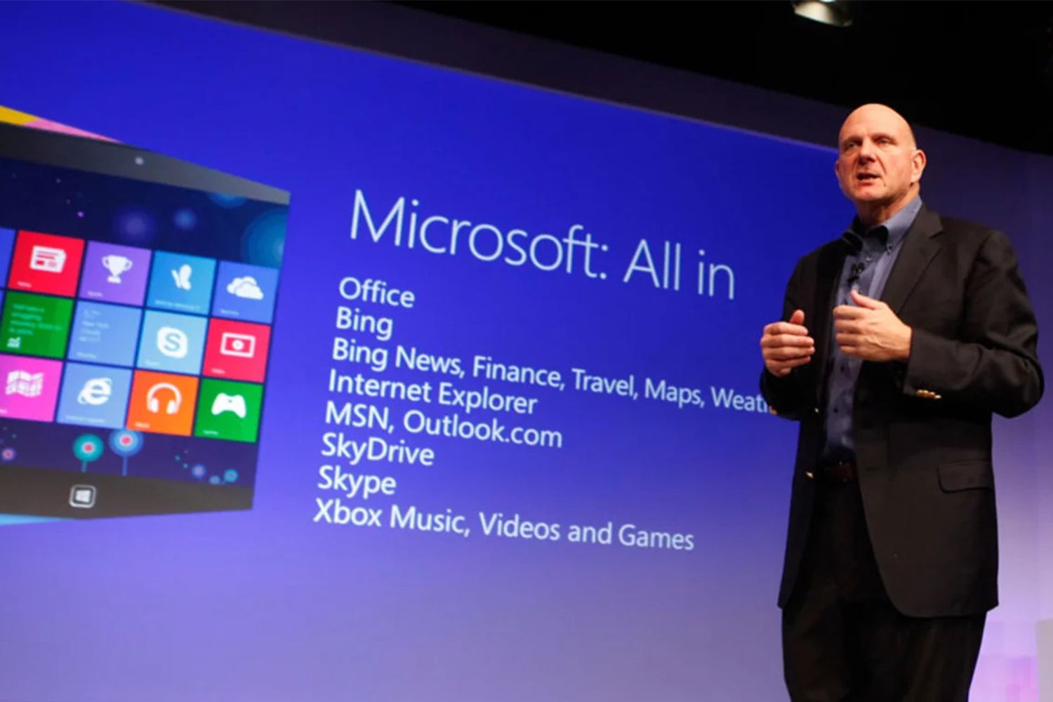 Man in suit presenting in front of a large screen, Microsoft debut graphics.