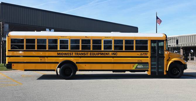 A full-size, 40-foot yellow school bus sits in a parking lot. Midwest Transit Equipment, Inc is written on the side and there is a SEA-Drive decal to the left of the door.