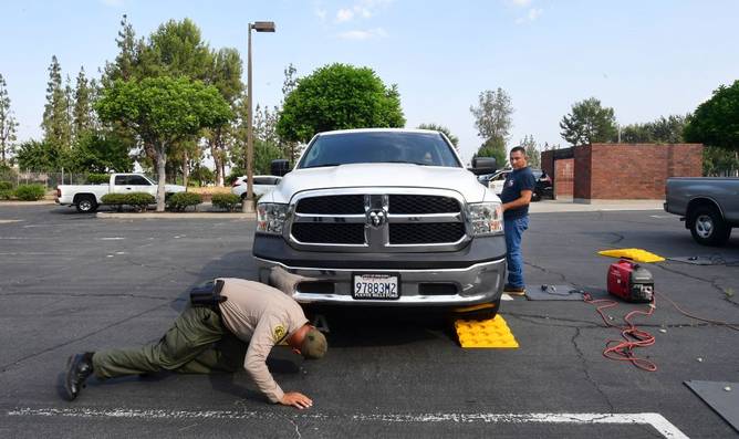 Deputy Jaime Moran (R) from the Los Angeles Sheriffs Department speaks with a driver as fellow officer checks the location of the catalytic converter beneath the vehicle for engraving with a traceable number on July 14, 2021, in City of Industry, California