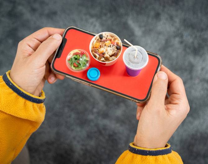 A photo-illustration where a smartphone resembles a food tray carrying soup, a salad, and a drink. 