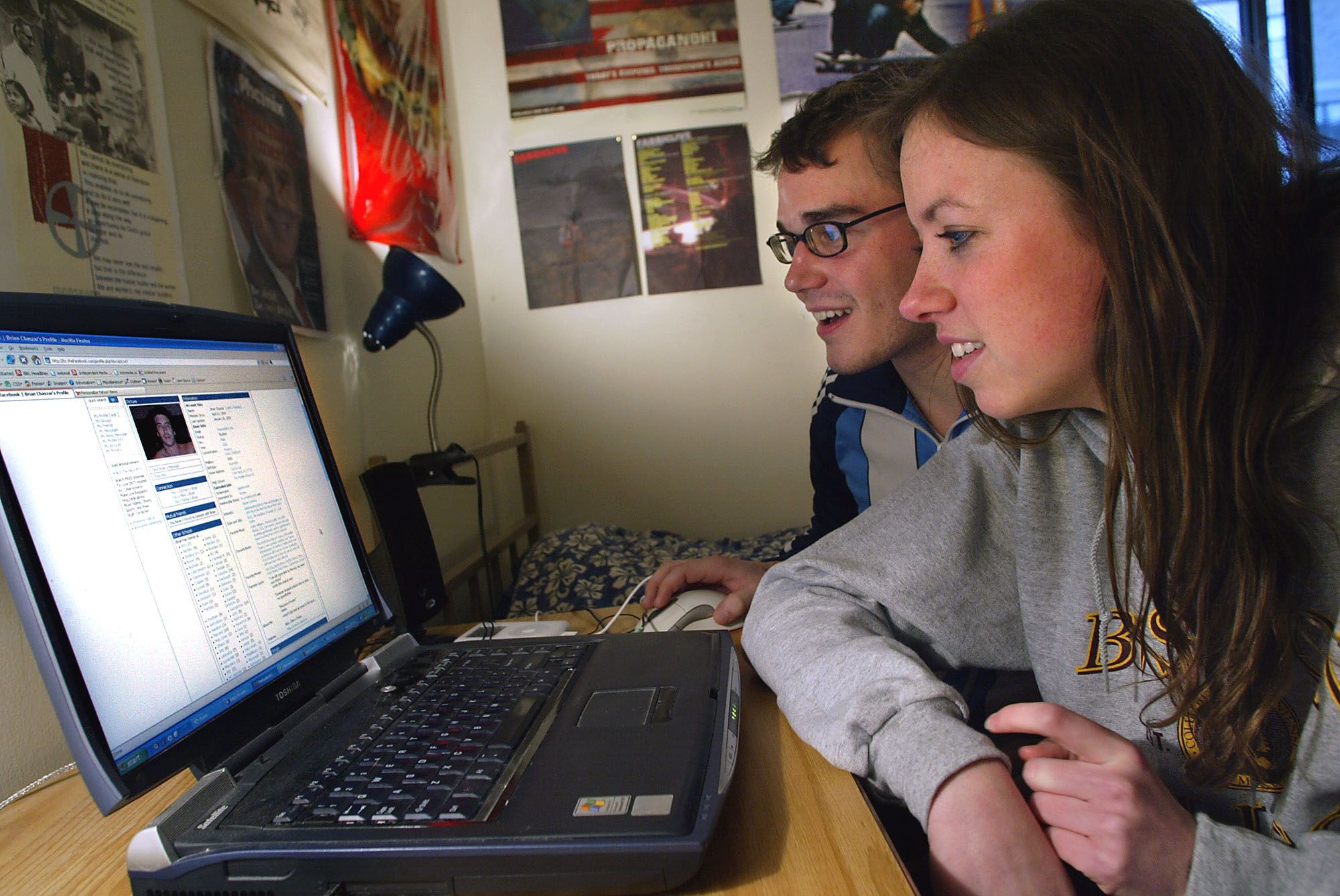 Two teenagers looking at an early iteration of facebook on a chunky laptop computer.