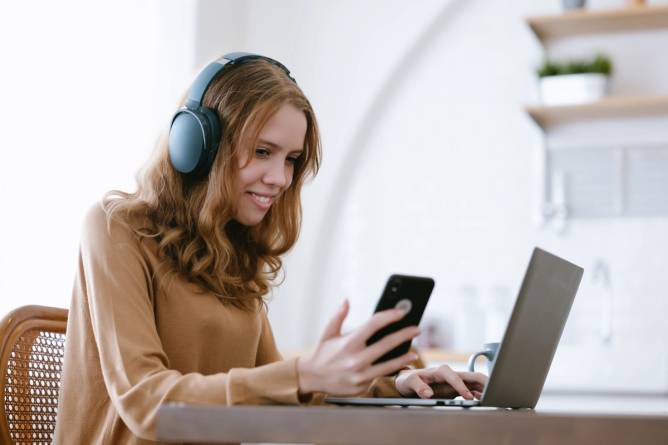 Image of a woman using a smartphone and a laptop simultaneously.