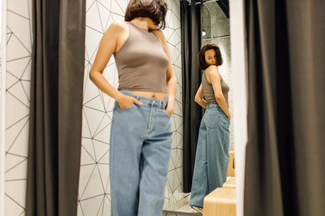 Woman checking herself in mirror while trying on new jeans.