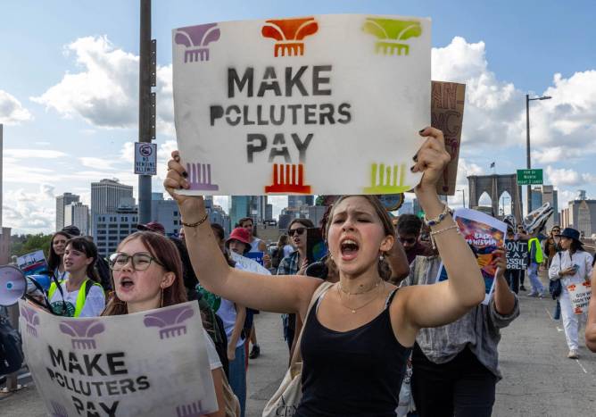 Youth activists hold signs that say "Make Polluters Pay," which New York recently passed a low to do.