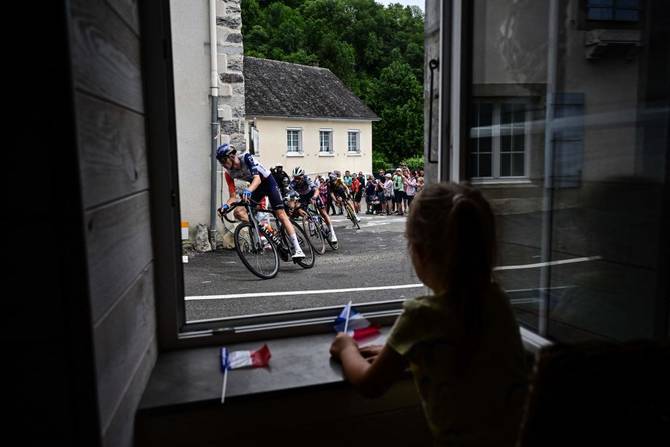 A little girl looks out a window as the pack of riders cycles past during the 5th stage of the 110th edition of the Tour de France