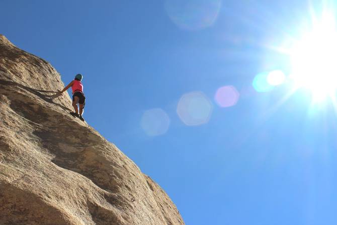 A person climbs the side of a cliff on a sunny day.