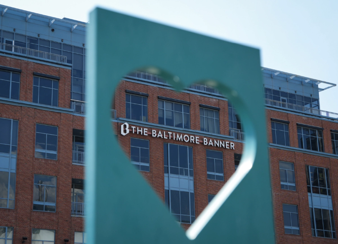 the Baltimore Banner on the side of a building framed by a blue heart statue in the foreground