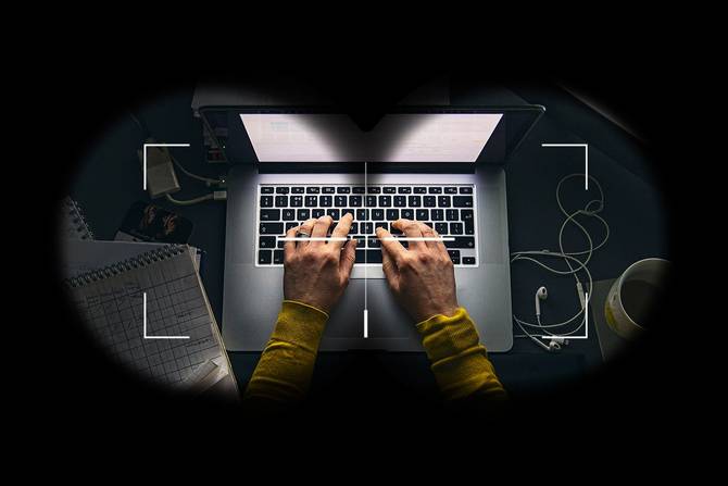 Hands type on a laptop viewed through spy binocolars