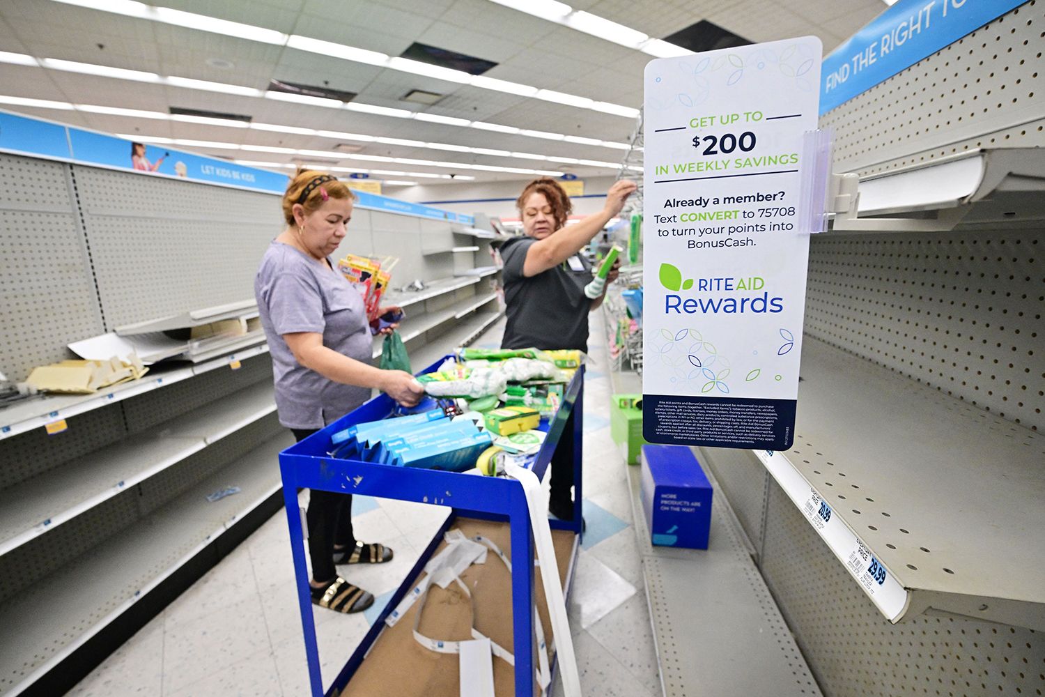 A woman browses through what items remain as an employee pulls items off near empty shelves at a Rite Aid store