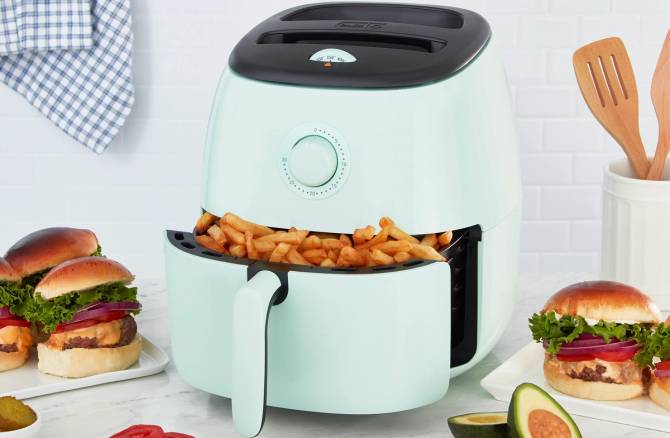 An open air fryer with fries inside on a countertop with burgers and avocados