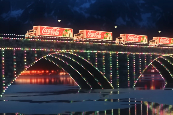 lighted Coca-Cola trucks on a lighted bridge at night